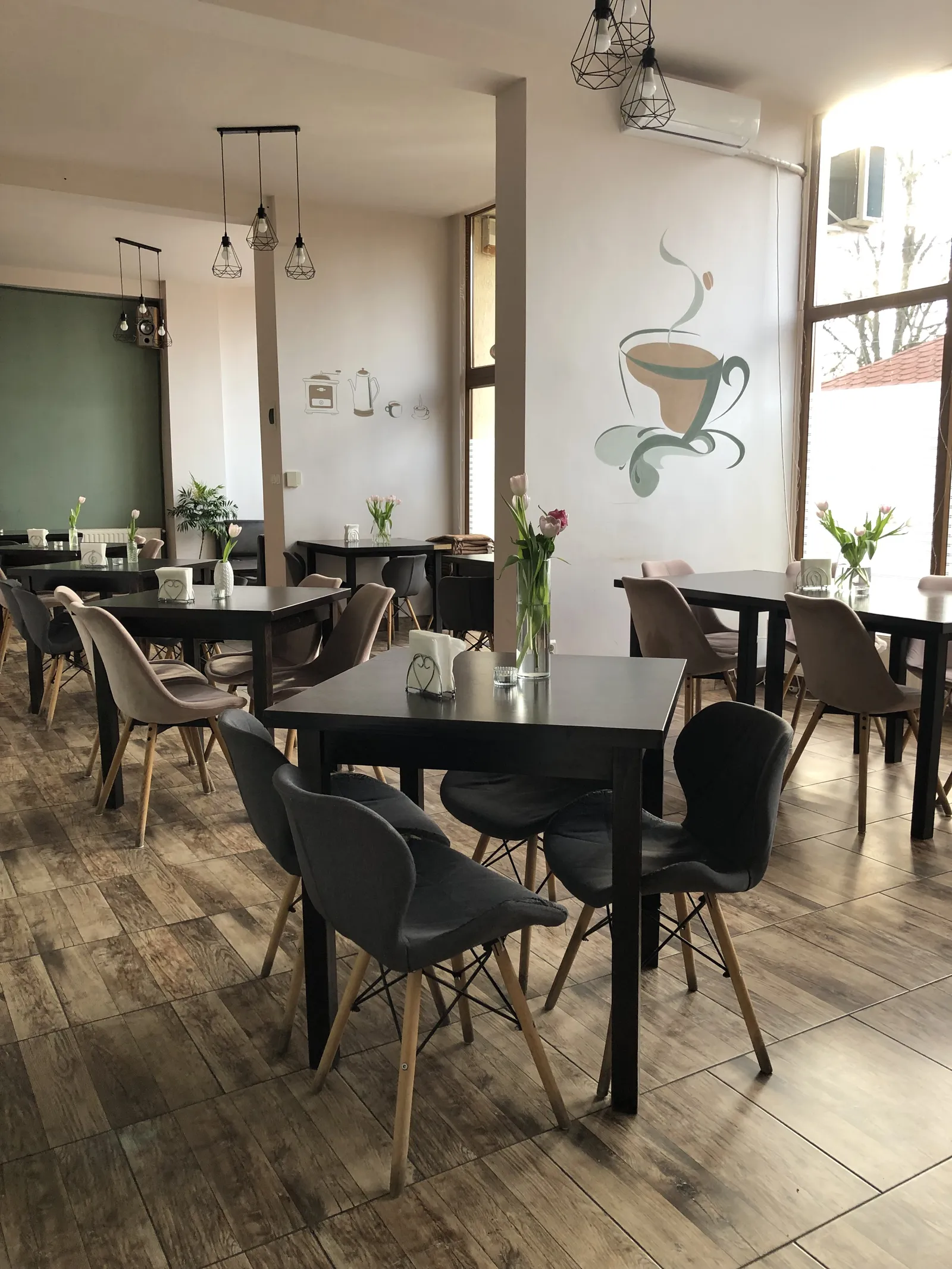 Sala de mese a bistroului: mese și scaune închise la culoare, în fața unei picturi murale cu o ceașcă de cafea