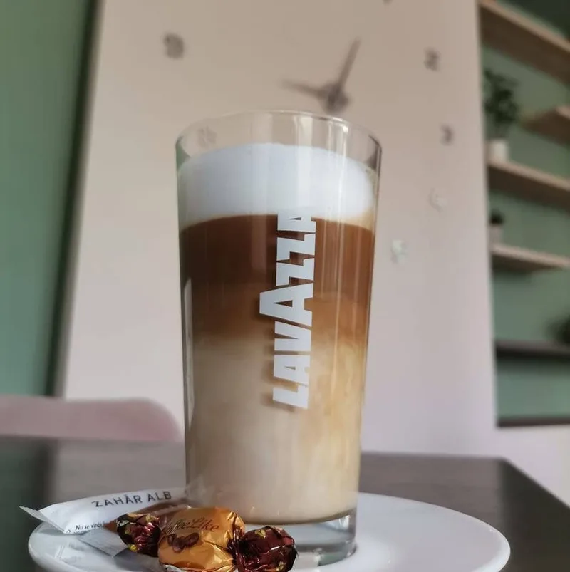 Un latte macchiato într-un pahar înalt, cu zahăr și bomboane pe farfurioară